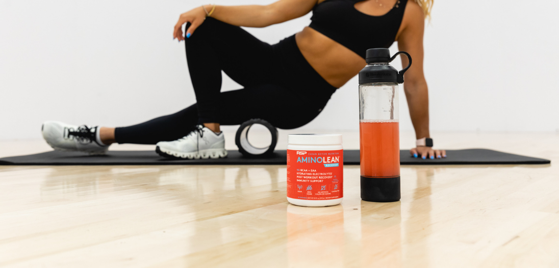 Woman foam rolling for post workout recovery while drinking amino lean recovery tropical island punch