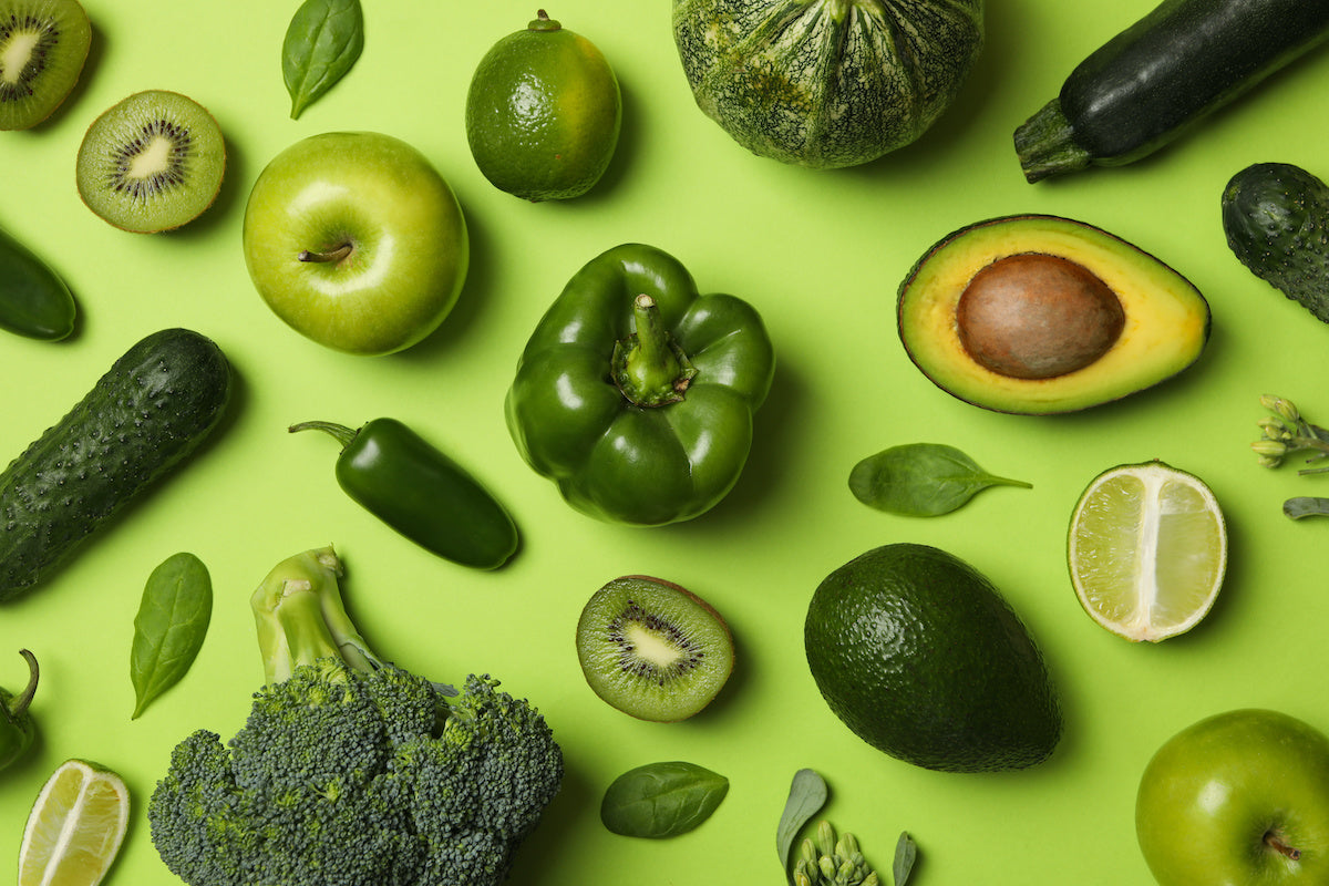 Healthy vegan greens including green pepper, avocado, apple, broccoli, spinach, and kiwi